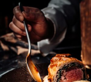 person holding stainless steel fork and knife slicing meat on black ceramic plate