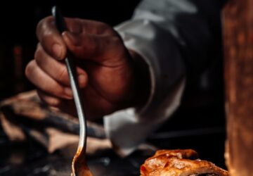 person holding stainless steel fork and knife slicing meat on black ceramic plate