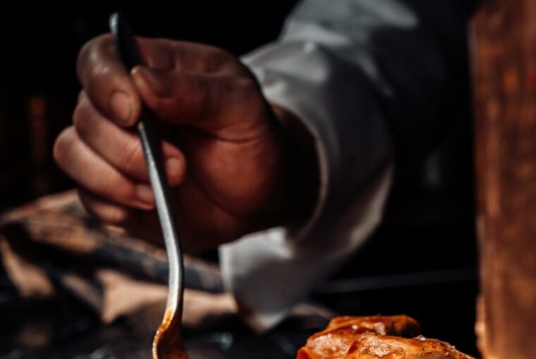 person holding stainless steel fork and knife slicing meat on black ceramic plate